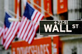A close-up of the sign for Wall Street is seen with the US flags on the New York Stock Exchange in the background in New York City, the US.
