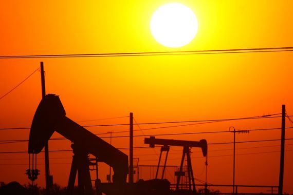 Silhouettes of oil wells under a bright sun against an orange sky