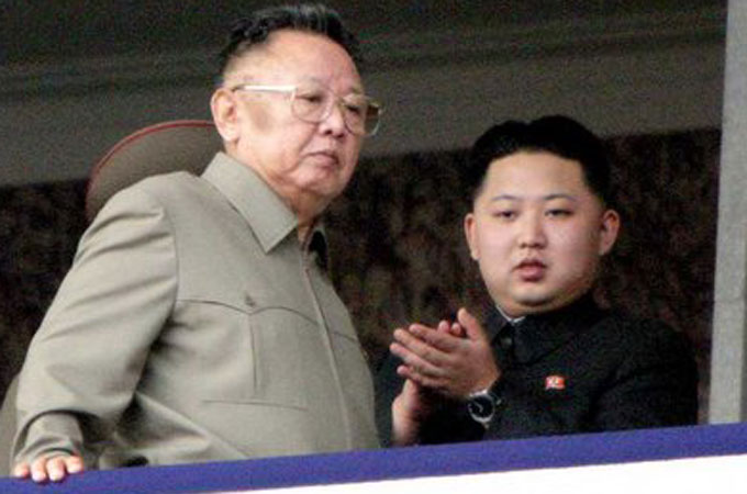 Kim Jong Il with Kim Jong Un standing behind him.