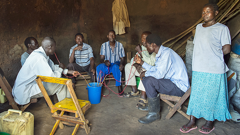 Drinkers enjoy a central pot of home-made alcohol in an illegal kafunda [AJ Heath/Al Jazeera]