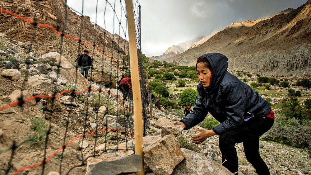 Tsering Angmo from the Snow Leopard Conservancy India Trust helps set up an electric fence to safeguard the village fields in Saspochey from wild species like Tibetan Blue Sheep. [Felix Gaedtke/NowHere Media /Al Jazeera]