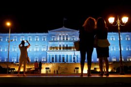 People stand in front of the parliament building illuminated in blue lighting in Athens, Greece [REUTERS]