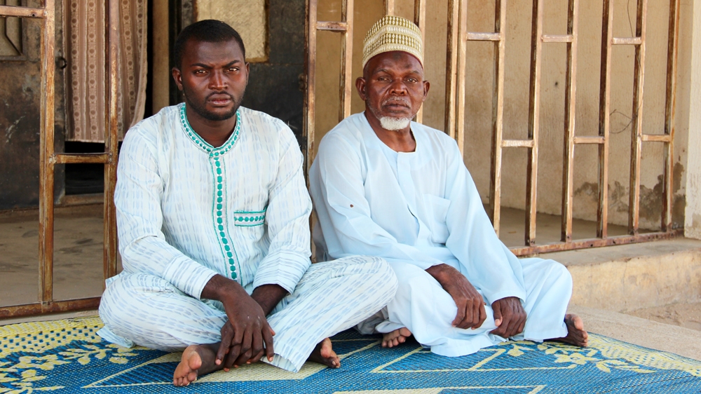 Aliyu's younger brother Abubakar and his father Mohammed in front of the family house where they used to sit in the shade [Femke van Zeijl/Al Jazeera] 