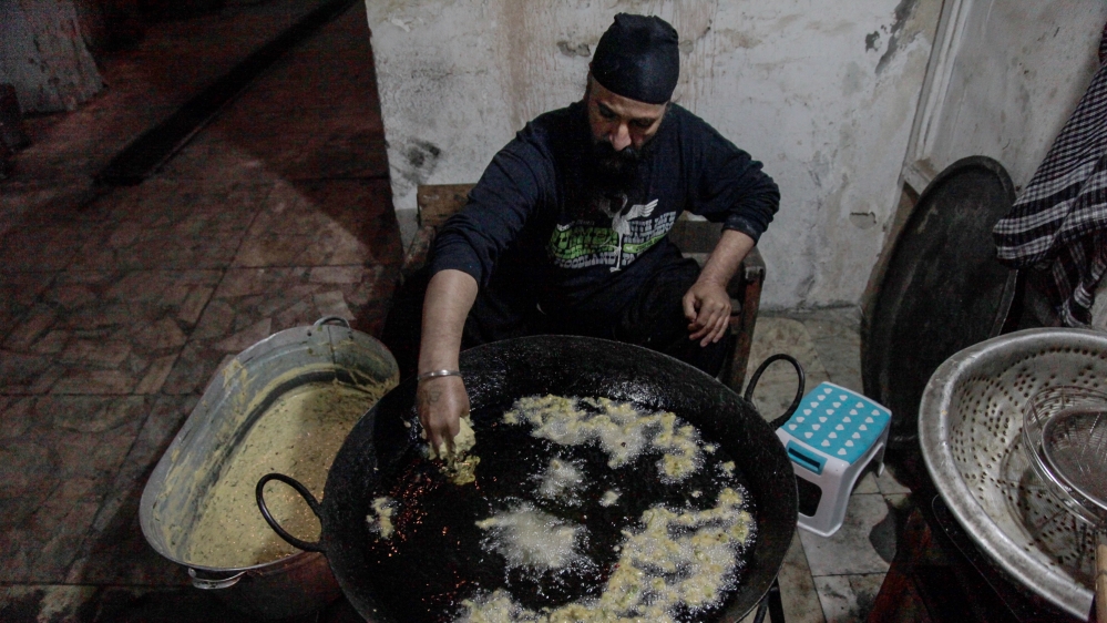 Sivender Singh, a gurudwara resident, drops the first batch of pakora batter into the hot oil just after 5am [Sune Engel Rasmussen/Al Jazeera]