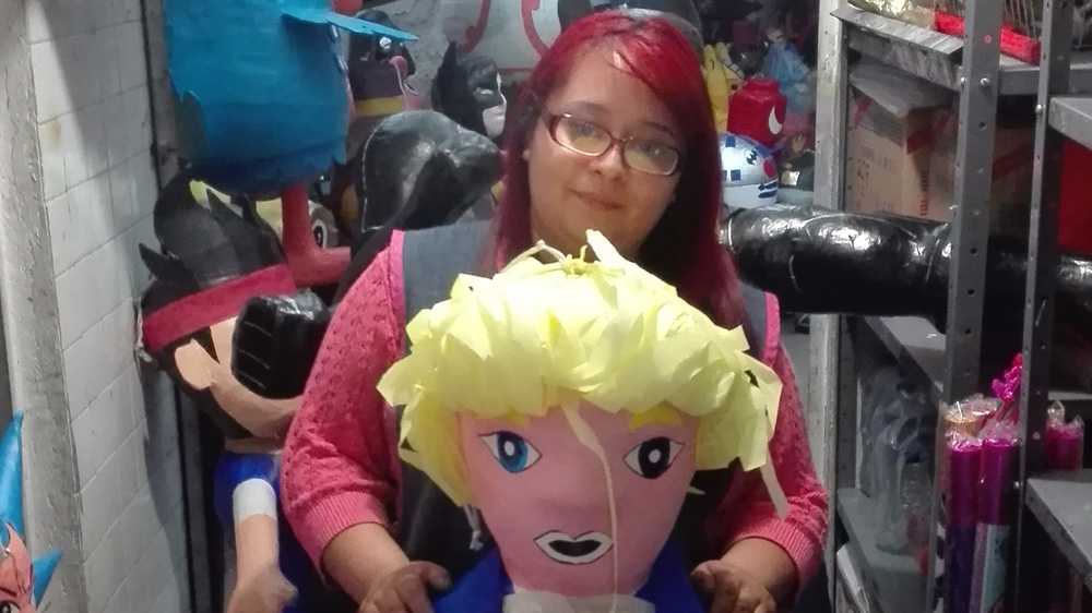 Fernanda Garcia, a pinata seller, poses with a Donald Trump model at the store where she works in Mexico City [Tim MacGabhann/Al Jazeera] 