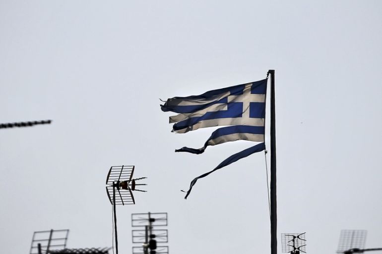 A frayed Greek national flag flutters among antennas atop a building in central Athens, Greece [REUTERS]