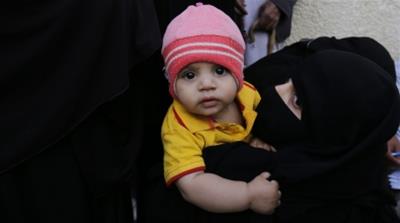 A Yemeni woman carries her child as she waits to receive a food ration provided by a local relief group in Sanaa [EPA]