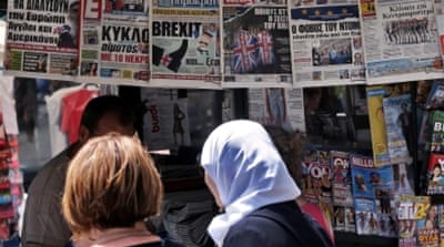 People glance at the front pages of Greek newspapers hanging on a kiosk in central Athens [EPA]