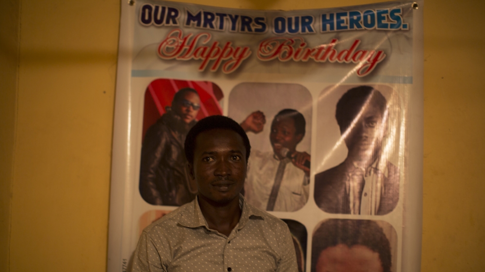Abdullah Mohammed in front of a poster showing three sons of Sheikh el-Zakzaky who were allegedly killed by the Nigerian army [Chika Oduah/Al Jazeera] 