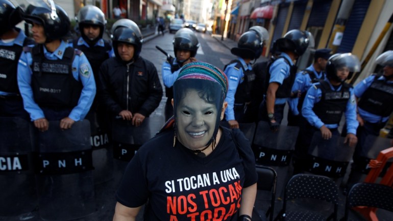 Demonstrator wearing a mask of slain environmental rights activist Berta Caceres stands in front of policemen during Honduran Women''s Day, which marks the women''s rights to vote and engage in politica