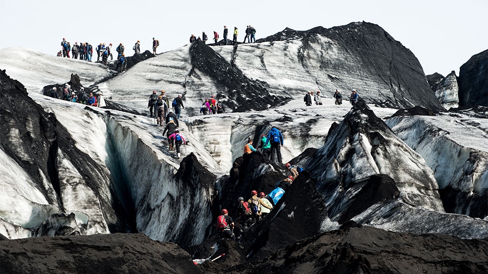 Groups of tourists on guided trips venture up the front of Solheimajokull glacier. Layers of black ash from the eruption of Katla volcano in 1918 are exposed as the ice melts away [Alexander Lerche/Al Jazeera]