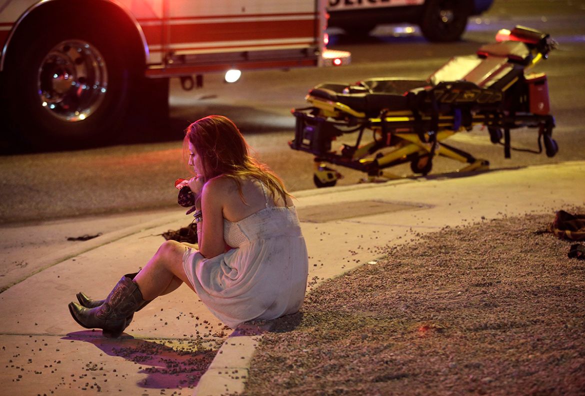 A woman sits on a curb at the scene of a shooting outside of a music festival along the Las Vegas Strip, Monday, Oct. 2, 2017, in Las Vegas. Multiple victims were being transported to hospitals after