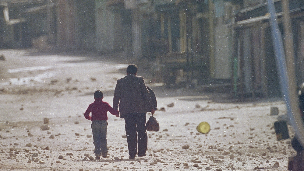A man holds his son's hand as they make their way along the debris littered street in the Balata refugee camp near Nablus in the occupied West Bank, December 11, 1987 [AP/Max Nash]