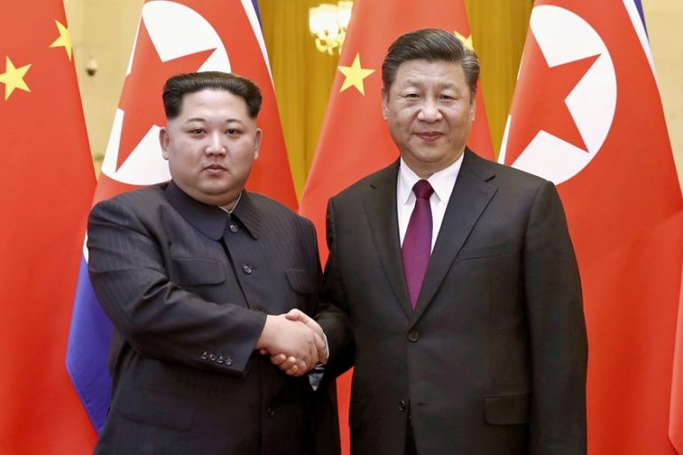 North Korean leader Kim Jong Un and Chinese President Xi Jinping shake hands in front of Chinese and North Korean flags in Beijing, China.