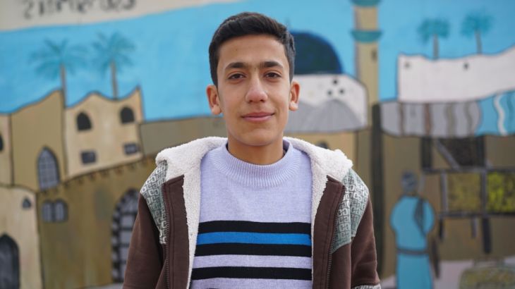 Mahmoud, 15 years old, as he stands in front of a mural in Zaatari refugee camp.