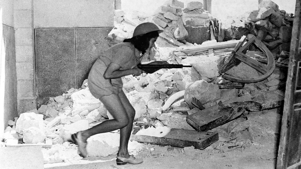 A Jewish fighter armed with a Sten gun picks her way through the shattered walls of Suleiman's Way, in the old city of Jerusalem, in 1948 [Jim Pringle/AP]