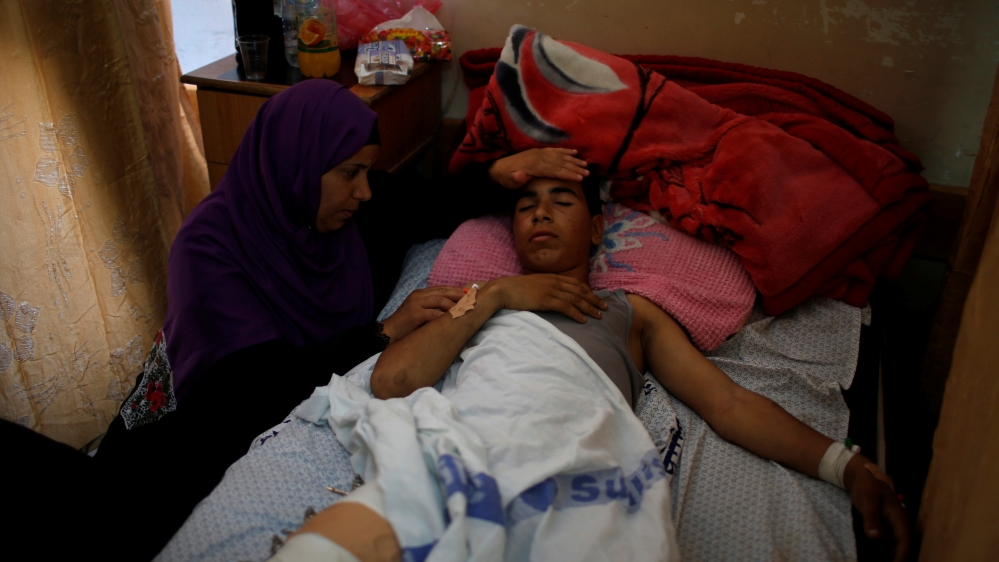 The mother of an injured Palestinian sits next to him as he lies on a bed at a hospital in Gaza City [Mohammed Salem/Reuters]