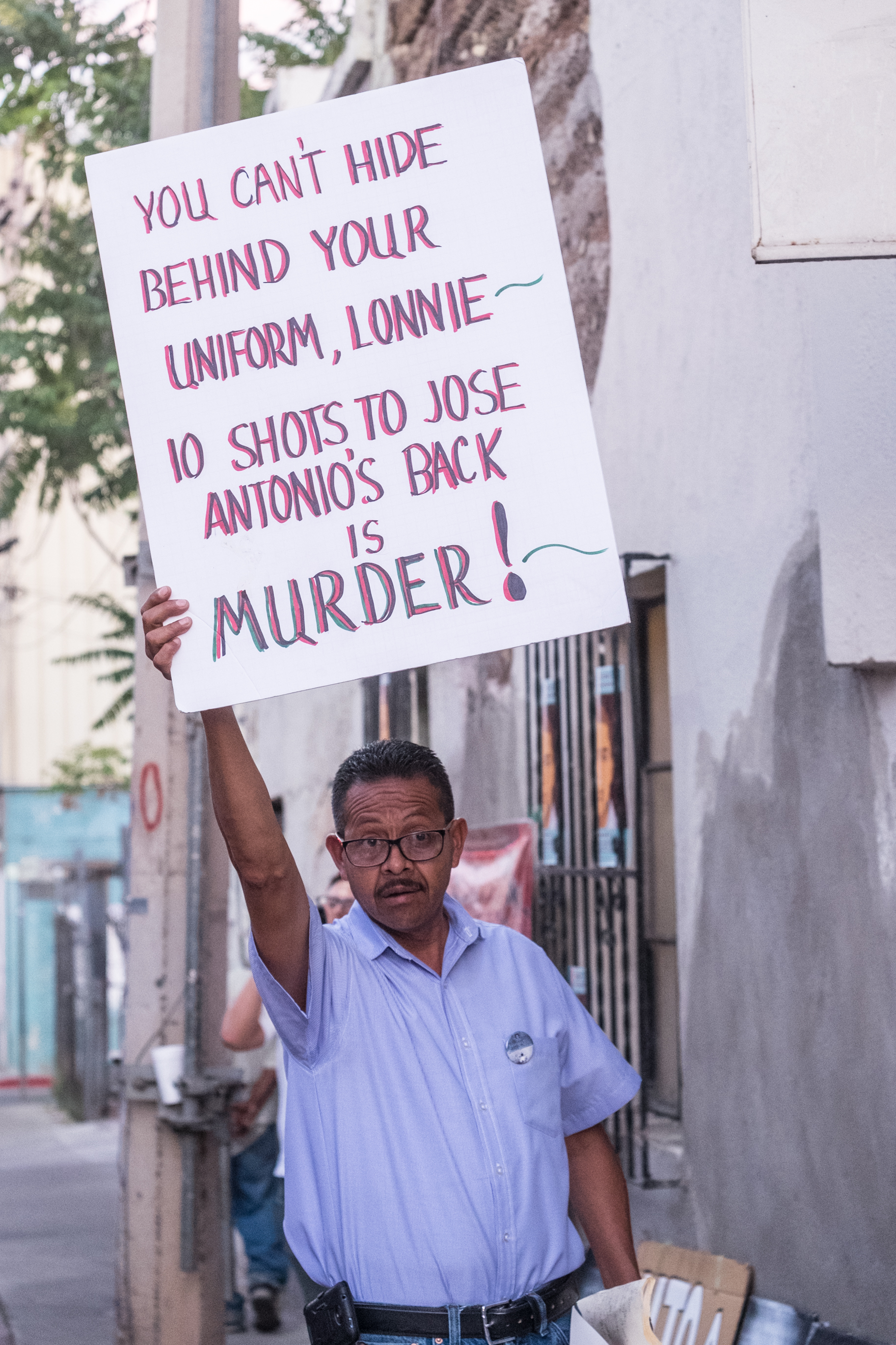Jose Raul Cuen Zojo, the uncle of slain Jose Rodriguez, holds up a protest sign for Border Patrol agents passing by in the car to read [Eline van Nes/Al Jazeera]