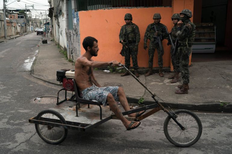 Soldiers on patrol watch a man pedal past on his tricycle at the City of God slum in Rio de Janeiro, Brazil, Thursday, June 7, 2018. More than five thousand soldiers and policemen took part in a surpr