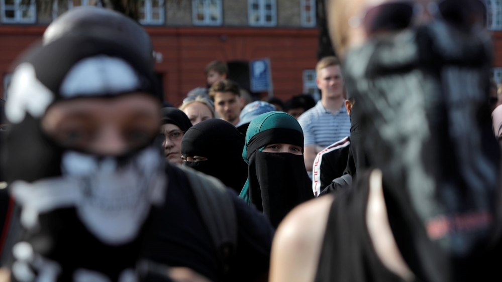 A woman in a veil stands among masked protesters in a demonstration against the Danish face veil ban in Copenhagen, Denmark, August 1, 2018 [File: Andrew Kelly/Reuters]