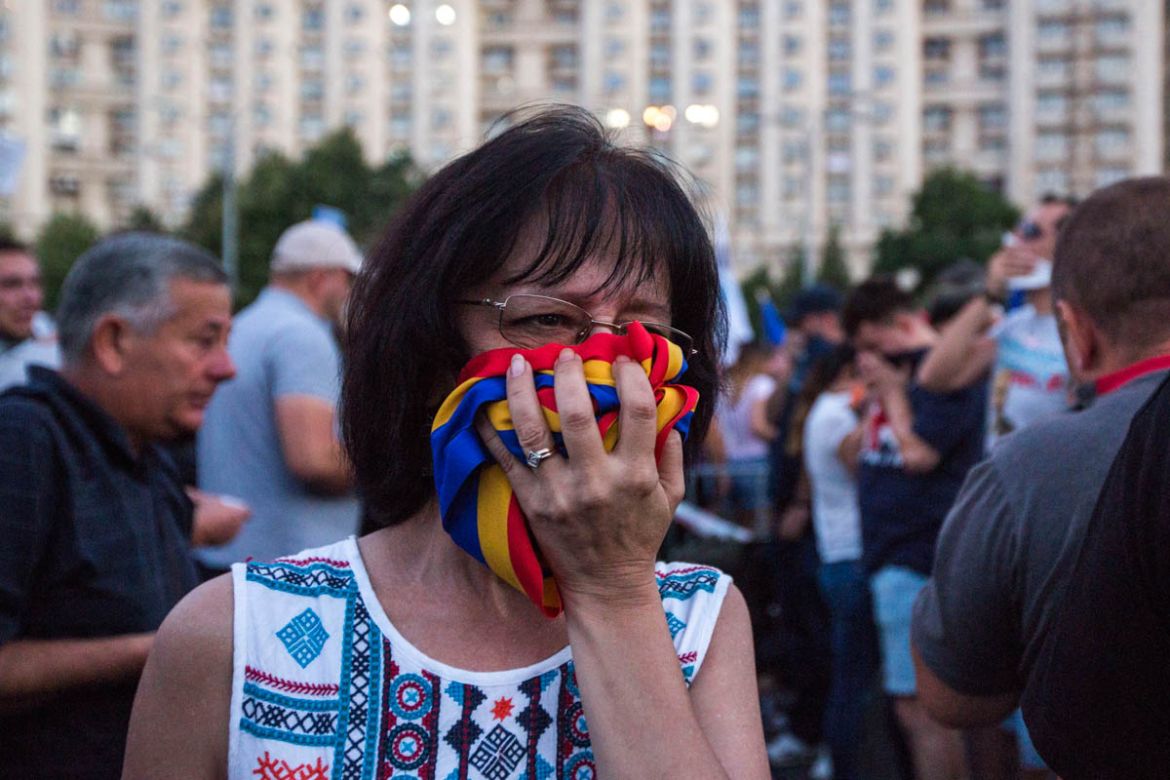 A woman covered her face with the Romanian flag after the riot police fired tear gas grenades towards the protesters. [Alexandra Radu/Al Jazeera]