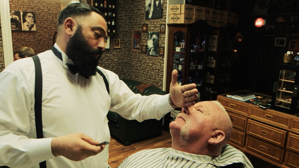 Hussein in his element, giving a customer a shave in his barbershop. [Al Jazeera]