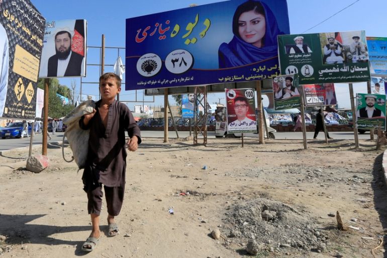 Election posters of parliamentary candidates are installed on a street while a boy walks past in Jalalabad