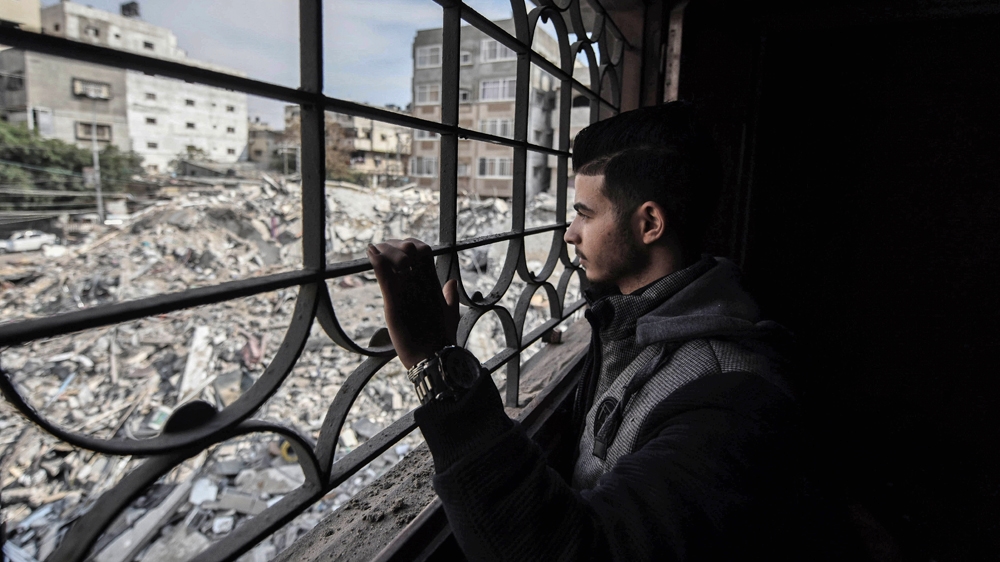Fadi looks out from his devastated apartment at rubble from the al-Rahma building [Walid Mahmoud/Al Jazeera]