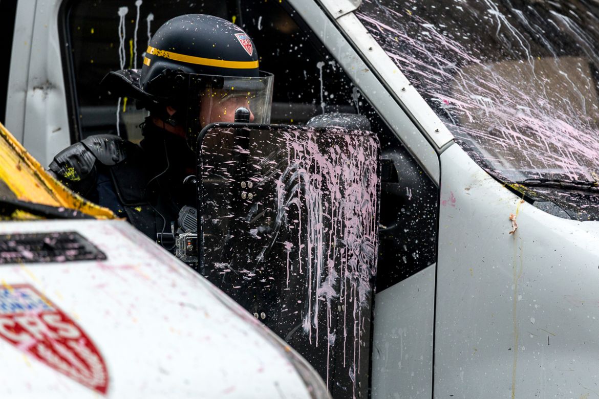 A police officer is seen behind riot gear on which protesters have thrown paint while gathering to control the situation during a protest on the adjacent streets to the Champs ElysE`es called for by t