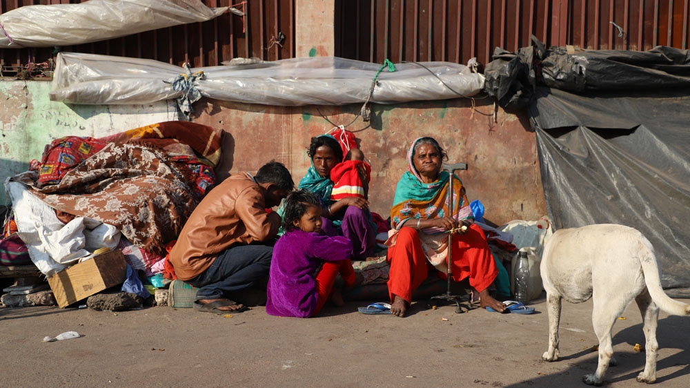 A group of homeless people is pictured while sitting on a pavement of a road in New Delhi [Nasir Kachroo/Al Jazeera]