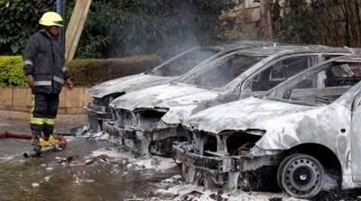 A firefighter stands near burned vehicles at the scene [Njeri Mwangi/Reuters]