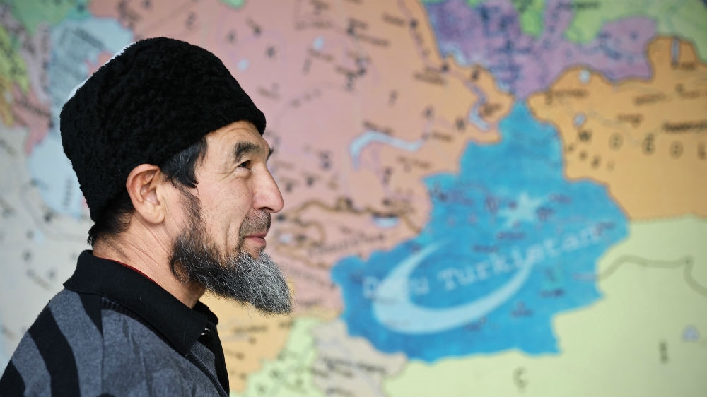 A Uighur man stands in front of a map showing Xinjiang, the Uighur homeland in China that some believe should be the independent state of East Turkestan [Steve Chao/Al Jazeera]