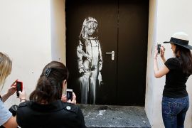 Young women take a picture of a recent artwork attributed to street artist Banksy on June 26, 2018 in Paris,