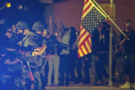 A police officer raises his weapon at a car speeding in his general direction as a more vocal and confrontational group of demonstrators stands on the sidewalk during further protests in reaction to t
