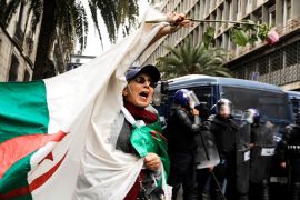 Police members stand guard as a woman carries a flower and a national flag during a protest against President Abdelaziz Bouteflika, in Algiers, Algeria March 8, 2019