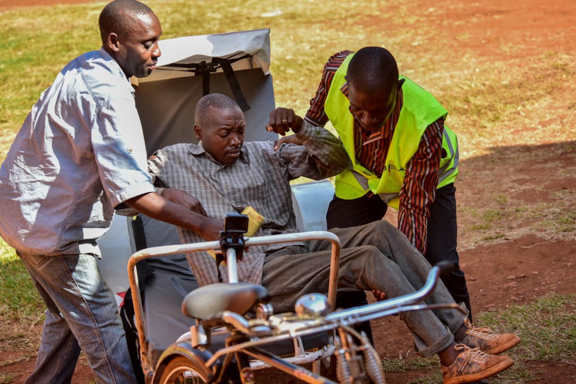 Mukasa Harid, a member of the Village Health Team alongside a native helps a patient temporarily crippled by excess alcohol into the ward at Budondo Health Centre. In Uganda, less than 7% of patients