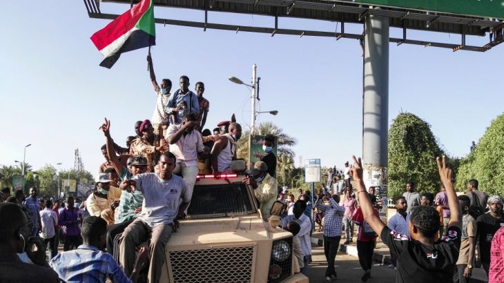 Sudanese protesters wave a national flag and flash the victory sign as they sit atop a military vehicle next to soldiers near the capital Khartoum''s military headquarters on April 7, 2019