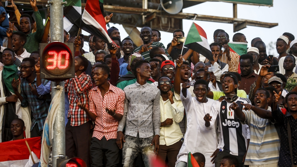 Sudanese men wave national flags and chant slogans as they gather outside the army headquarters in Khartoum [Ashraf Shazly/AFP]