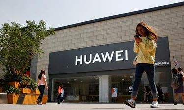 A woman looks at her phone as she walks past a Huawei shop in Beijing, China May 16, 2019. REUTERS/Thomas Peter