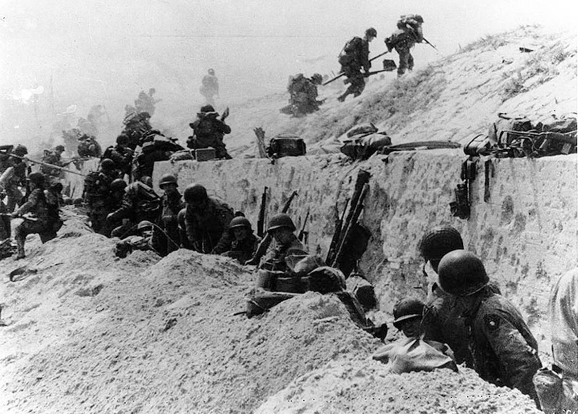 U.S. Army soldiers of the 8th Infantry Regiment, 4th Infantry Division, move out over the seawall on Utah Beach after coming ashore in front of a concrete wall near La Madeleine, France, June 6,1944,