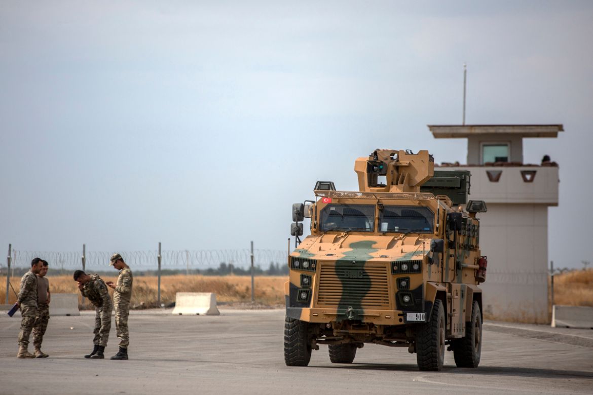 Turkish troops stand and speak near an army tank positioned directly in front of the Karkamis border crossing