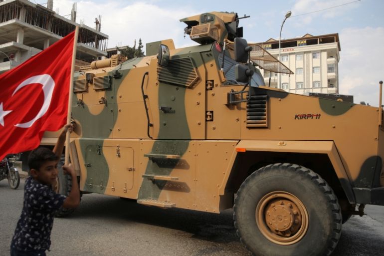 Boy waves a Turkish flag as Turkish military vehicles drive on a street in the Turkish border town of Akcakale