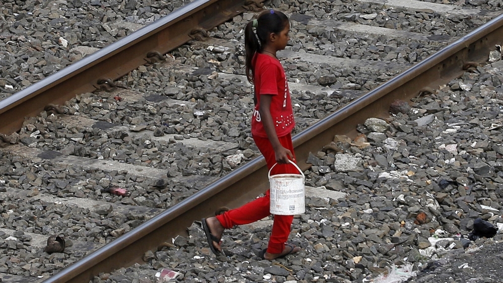 In this June 30, 2015 file photo, an Indian girl holds a can filled with water and walks past railway tracks to defecate in the open in Mumbai, India. The numbers in the government's ambitious Swachh 