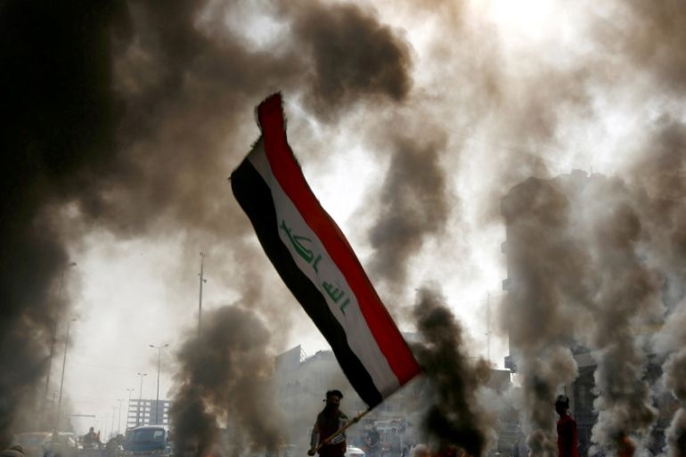 FILE PHOTO: A protester holds an Iraqi flag amid a cloud of smoke from burning tires during ongoing anti-government protests in Najaf, Iraq November 26, 2019. REUTERS/Alaa al-Marjani/File Photo