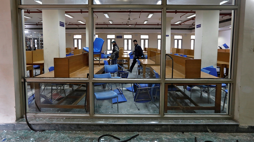 People walk inside a partially damaged library of the Jamia Millia Islamia university after police entered the university campus on the previous day, following a protest against a new citizenship law,
