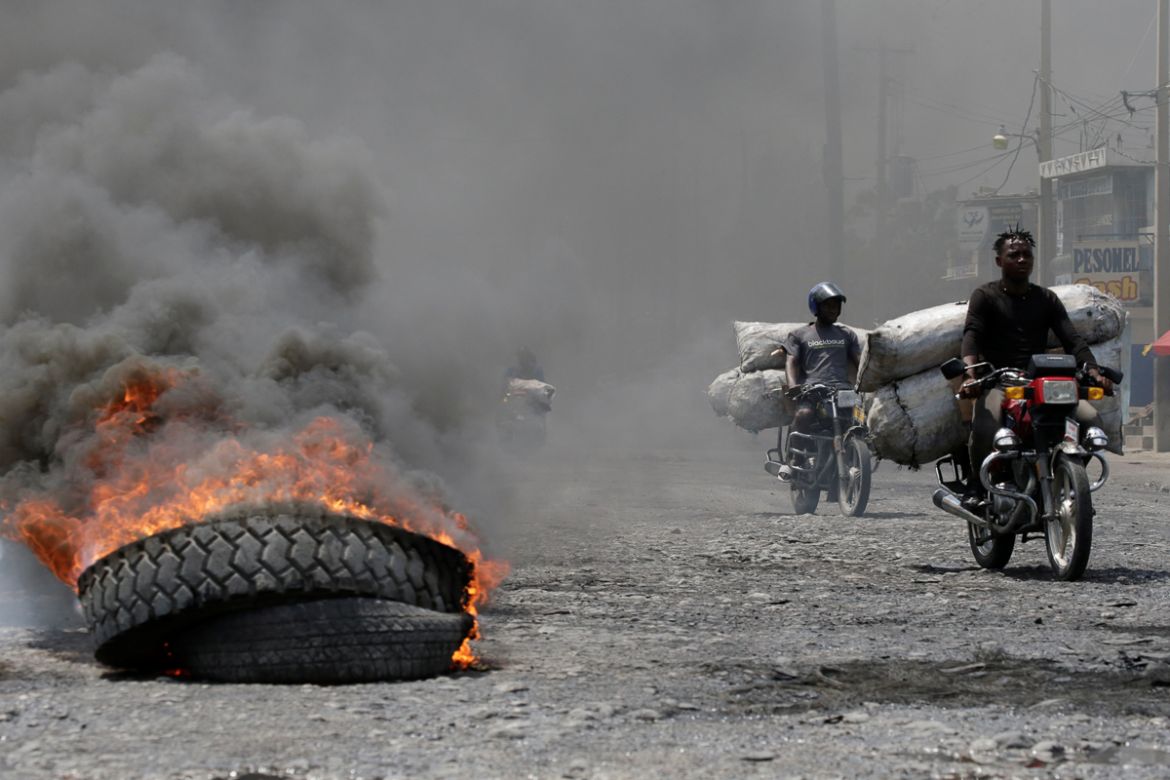 Men riding motorbikes pass next to a burning tire at a barricade in a street of Port-au-Prince, Haiti October 2, 2019. REUTERS/Andres Martinez Casares