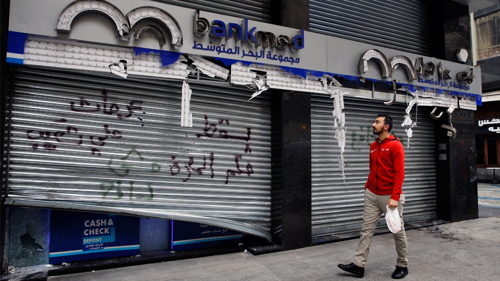 A man passes by the broken facade of the Bank MED that was smashed by anti-government protesters with a message that reads in Arabic, 