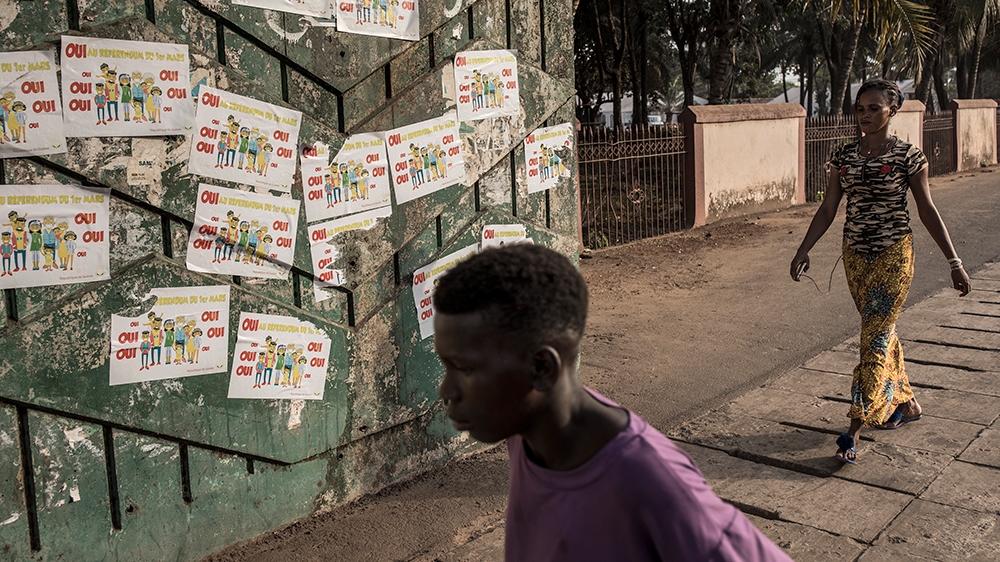 Guineans walk in front of posters advertising 