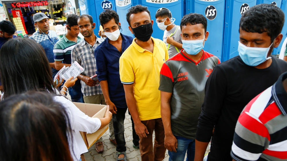 Migrant workers, mostly from Bangladesh, queue to collect free masks and get their temperatures taken in Singapore