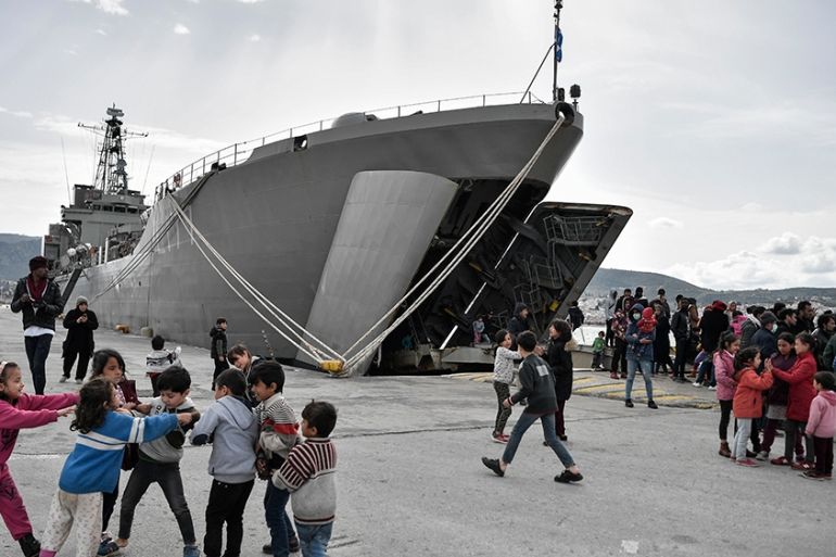 Children play past the military carrier which accomodates refugees and migrants arrived on Lesbos island after March 1, in the port of Mytilene on the island of Lesbos on March 7, 2020. (Photo by LOUI